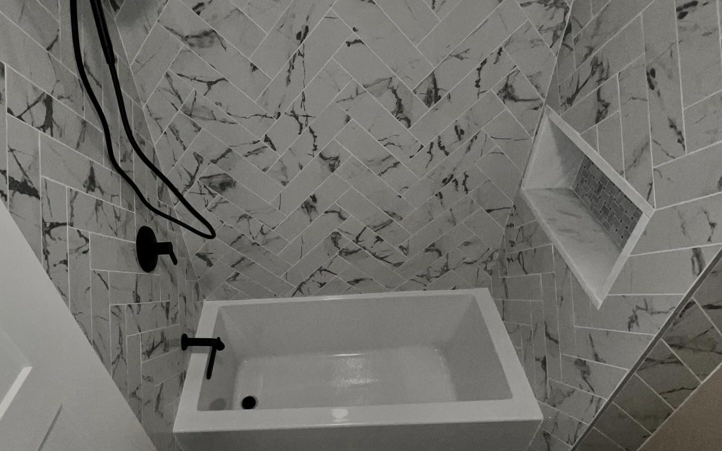 Marble-look tub surround with a tiled niche and matte black fixtures